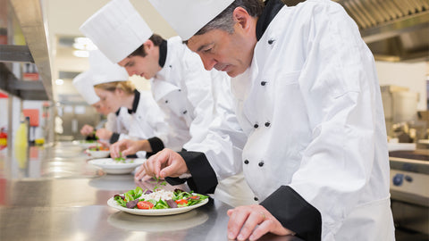 Chefs in a kitchen preparing food with a logo for 'n Italian chefs' favourite oil brand' in the corner.