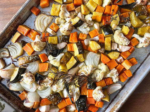 Roasted vegetables on a baking tray including carrots, onions, and cauliflower.